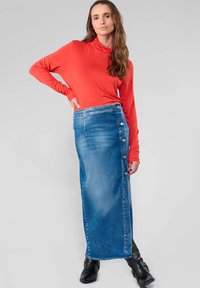 Jupe en denim, bleue, longueur genou avec fermeture à boutons sur le côté, associée à un haut rouge à manches longues. Texture lisse, silhouette ajustée.