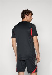 Svart sporttröja med röda accenter och korta ärmar, kombinerad med svarta shorts med röda detaljer och tre vertikala ränder.