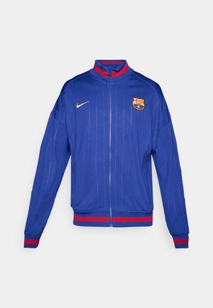 Blue zip-up jacket made of smooth fabric with vertical pinstripes, featuring red and gold accents, and an embroidered team logo on the chest.