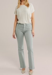 Haut gris clair à manches courtes associé à un jean vert clair ajusté. Le jean présente une coupe droite, avec des poches et une texture subtile.