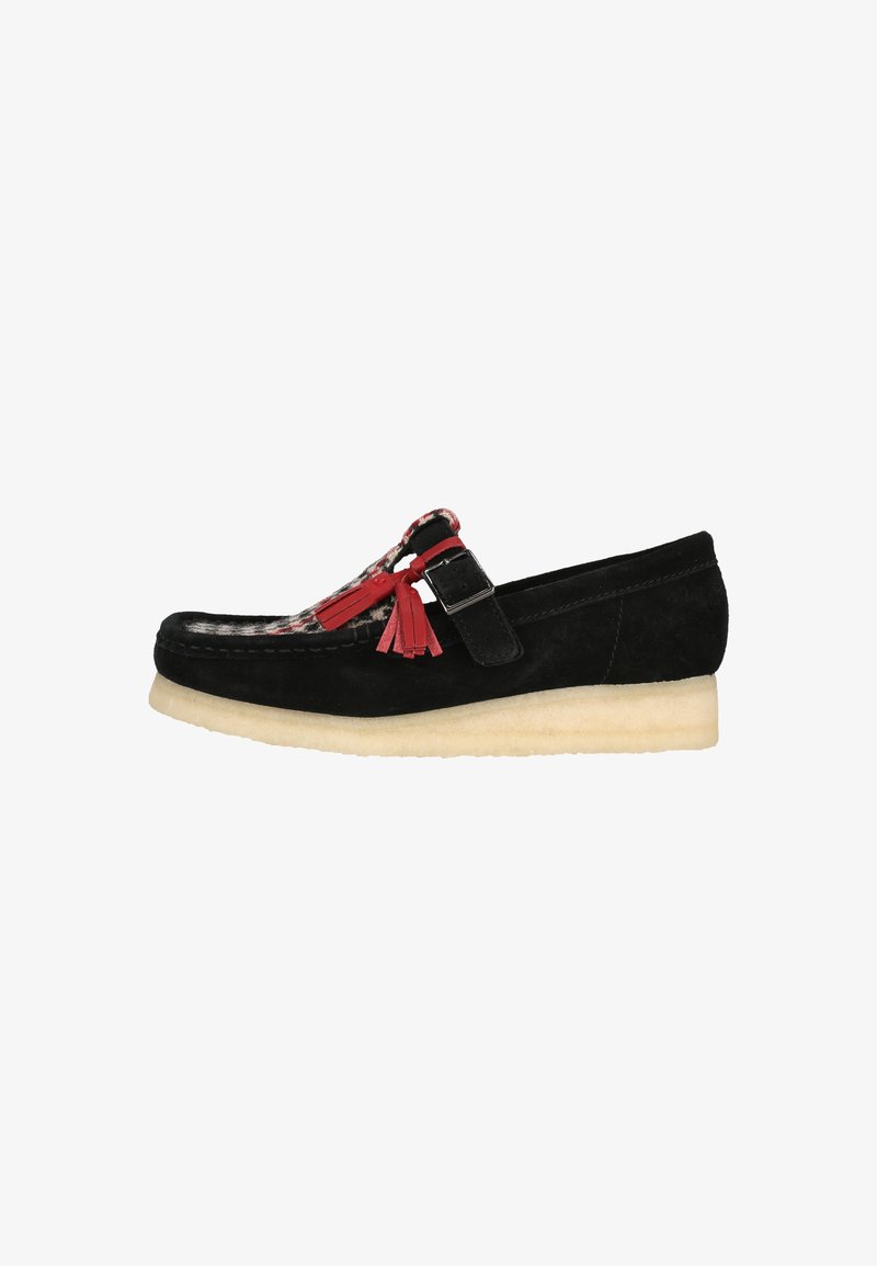 Schwarze Wildleder-Slipper mit runder Zehenpartie, kontrastierendem roten Karostoff und dekorativen Quasten. Leichte, strukturierte Sohle für besseren Halt.