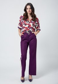 Koszula w kwiaty na guziki w kolorze białym, czerwonym i fioletowym; luźny krój. Fioletowe spodnie proste z regulowanym paskiem i kremowymi paskami po bokach.