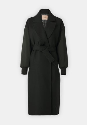 Fekete kabát, szabott gallérral, övvel hangsúlyozott derékkal és hosszú, puffos ujjakkal. Anyagának keverékéből készült, texturált bélés jellemzi.