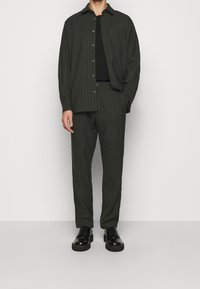 Mörkgrön skjorta med randig design, knappar och bröstficka, matchad med byxor i samma material och svarta snörskor. Slät textur.