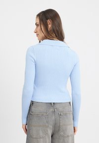 Suéter de malha canelada azul claro com colarinho, corte justo e mangas longas, combinado com jeans cinza de cintura alta com bolsos traseiros.