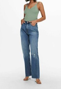 Top verde a costine con scollo a V, abbinato a jeans blu a gamba dritta con vita alta e dettagli strappati. Sandali con tacco trasparente.