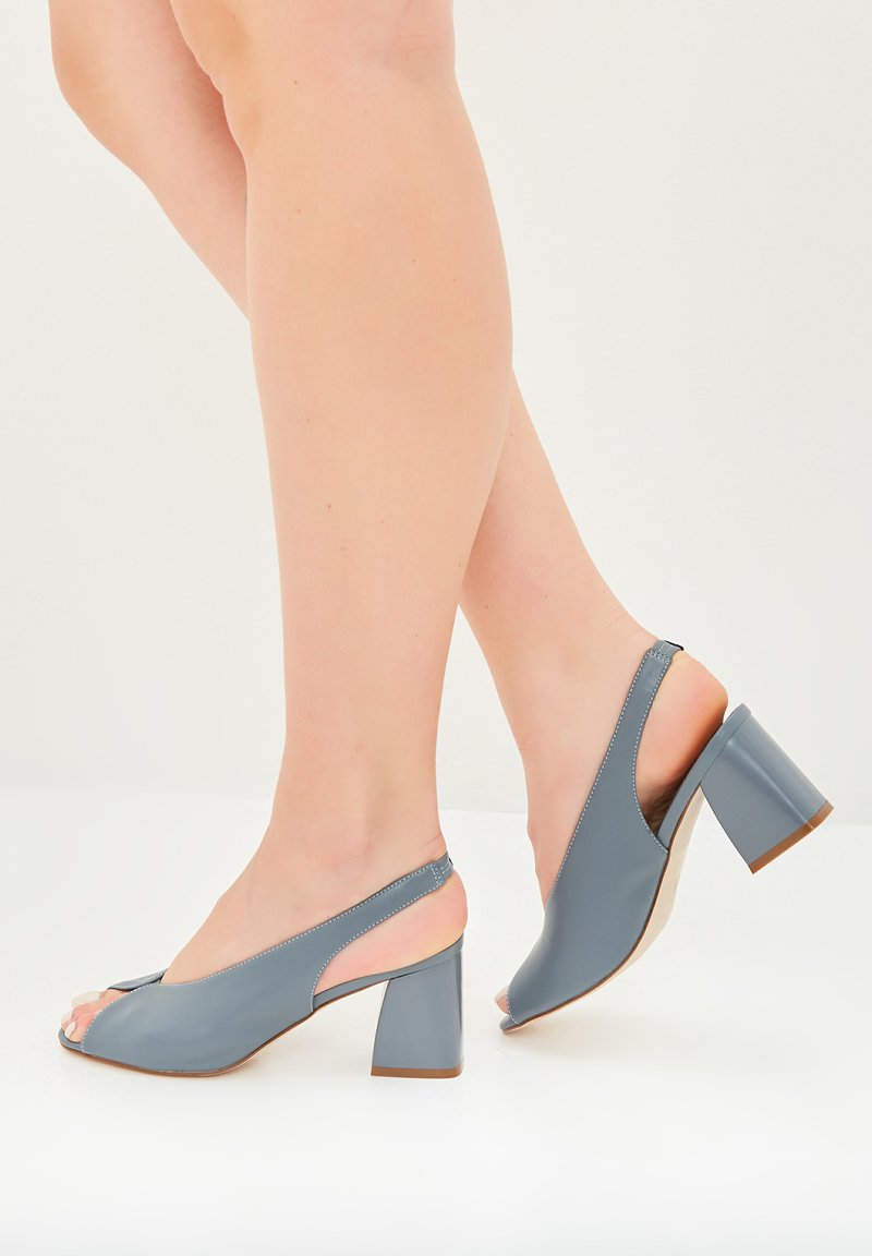 Scarpe slingback grigie in pelle con apertura a piedi e tacco a blocco, arricchite da accenti nudi a contrasto. Texture liscia e design pulito con cuciture minimali.