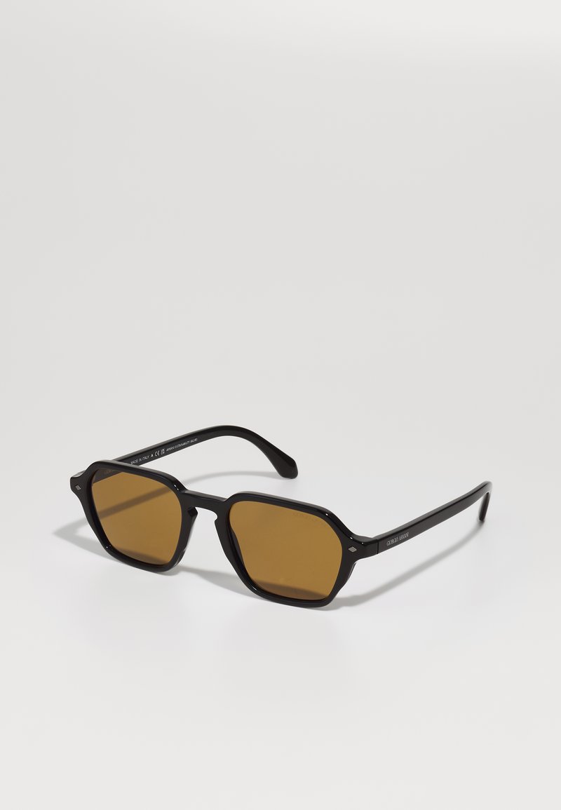 Ochelari de soare negri cu un ramă geometrică, lentile maro cu nuanțe, și accente subtile pe sprijină. Textură netedă și design ușor.