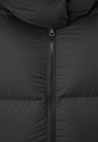 Fekete puffertotó középső cipzárral, steppelt textúrával és magas gallérral. Puha, szigetelt anyag a melegség érdekében.