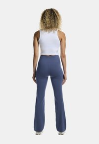 Biały krótki top bez rękawów i niebieskie o wysokim stanie, rozszerzające się spodnie. Materiał wydaje się gładki i sportowy w designie. Brak widocznych wzorów lub elementów metalowych.