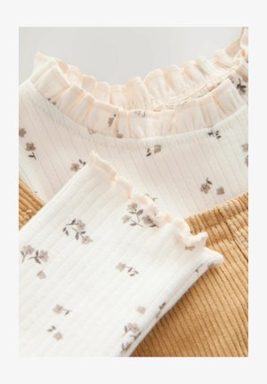 Twee gelaagde stofmonsters: de ene met een gerimpelde pastelkleurige kraag en een bloemmotief, de andere in gestructureerd mosterdkleurig corduroy.