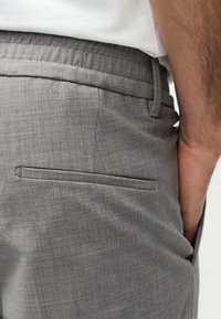Close-up of a person wearing grey tailored trousers with a slim back pocket and a white tucked-in shirt.