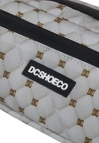 Torba na rzeczy DC Shoes wykonana z szarego materiału z pikowanym wzorem, z czarnymi zamkami błyskawicznymi i białą naszywką z logo.