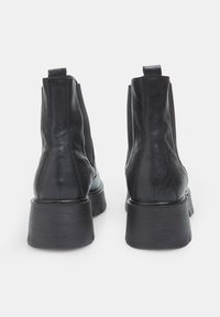 Botas negras de cuero hasta el tobillo con un tacón robusto, paneles laterales elásticos y una textura suave. Diseño minimalista sin detalles de marca visibles.