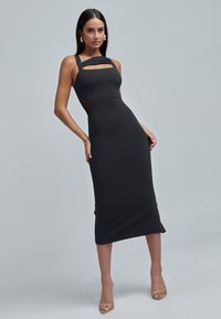 Musta bodycon-mekko leikkauksilla ja leveillä hihnoilla, jossa on sileä pinta ja keskipitkä helma, täydentäen alastonkorot.
