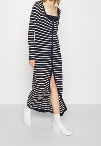 Pletené dlouhé šaty s námořnickými a bílými pruhy; mají čtvercový výstřih, dlouhé rukávy, přední knoflíky a rozparek až ke stehnům. Nosené s bílými teniskami.