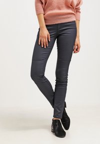 Pantaloni in ecopelle blu con un design aderente, caratterizzati da una texture liscia e dettagli di cucitura sottili, abbinati a stivali neri alla caviglia.