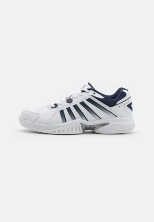 Baskets blanches avec des accents navy, présentant un dessus perforé, des rayures sur les côtés et une semelle texturée pour l'adhérence et le soutien.