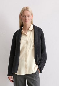 Dunkelgrauer gerippter Cardigan mit Schalkragen, langen Ärmeln und offenem Design, kombiniert mit einer hellgelben Knopfleiste.