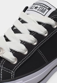 Μαύρο αθλητικό παπούτσι Converse All Star με λευκά χοντρά κορδόνια, λευκή ραφή και λευκή λαστιχένια σόλα ορατή στην περιοχή της μύτης.