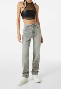 Top corto halter de malla negra combinado con jeans de pierna recta de talle alto en gris claro y zapatillas blancas. Presenta costuras m�ínimas y bolsillos.