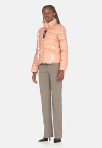 Giacca a vento lucida rosa con colletto alto e chiusura con zip, abbinata a pantaloni grigi chiari e tacchi neri.