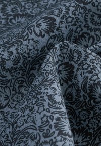 Tessuto blu a motivo con superficie texturizzata, caratterizzato da disegni floreali scuri e dettagli intricati, che creano un aspetto stratificato.