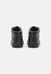 Scarpe alte in pelle nera con colli imbottiti, chiusure con zip sul retro, dettagli testurizzati e logo del marchio evidenziato sulla suola.