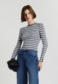 Gestreift in Grau und Weiß, langärmliges Oberteil mit gerippter Textur, kombiniert mit hochtaillierten blauen Jeans und einer schwarzen Clutch.