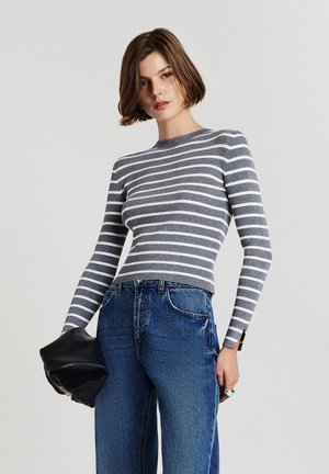 Gestreift in Grau und Weiß, langärmliges Oberteil mit gerippter Textur, kombiniert mit hochtaillierten blauen Jeans und einer schwarzen Clutch.