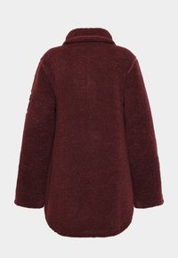 Burgundyröd, mjuk fleecekappa med krage, sänkta axlar och rundad fåll. Har en mjuk, texturerad yta för värme.