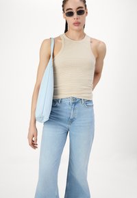 Μπεζ ριγέ μπλουζάκι με φαρδιές τιράντες, μπλε τσάντα ώμου και φθαρμένα μπλε καμπάνα τζιν. Λείες υφές, χαλαρή εφαρμογή και ανοιχτά χρώματα.