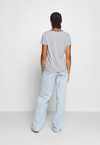 Randig kortärmad t-shirt i marinblå och vit, i kombination med ljusblå vida jeans, visad bakifrån. Slätt tyg och avslappnad passform.