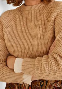 Paksu neulepaita beige värissä, jossa on ribbikuvio, pyöreä kaula-aukko ja raglan-hihat. Päälle kerros vaaleaa paitaa, jossa on pitkät hihansuut.