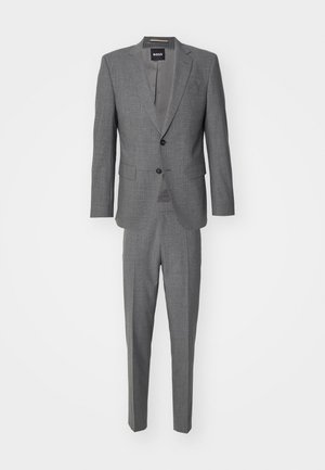 Pilkas kostiumas su tekstūruotu švarku, turinčiu dviejų mygtukų užsegimą, ir atitinkančiomis liesomis kelnėmis. Etiketė rodo "BOSS."