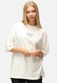 Bílý oversized tričko vyrobené z bavlny, se šedým logem "Looney Tunes" na hrudi a krátkými rukávy. Dolní lem je mírně zakřivený.