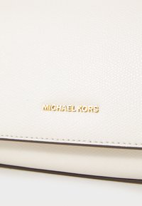 Portefeuille en cuir écru avec surface texturée, arborant le logo "Michael Kors" en dorure et des surpiqûres foncées contrastantes.
