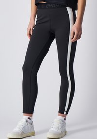Leggings negras deportivas con rayas blancas en los laterales, un diseño ajustado y una cinturilla alta. Combinados con zapatillas blancas y calcetas deportivas.