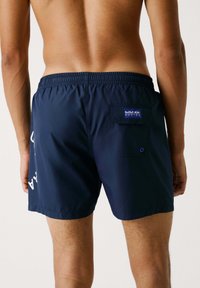 Costumi da bagno blu navy realizzati in tessuto leggero, dotati di una fascia elastica in vita, tasca posteriore e un patch con logo.