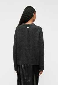 Σκούρο γκρι πλεχτό πουλόβερ με ψηλό λαιμό, ριγωτό στρίφωμα και κατακόρυφες ραφές στην πλάτη. Η υφή είναι μαλακή και χοντρή, με μια διακριτική ετικέτα λογότυπου.