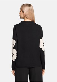 Czarny wełniany sweter z długimi rękawami, ozdobiony dużymi białymi kwiatowymi wzorami na rękawach oraz prostym okrągłym dekoltem. Gładka tekstura.