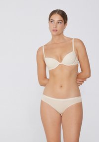 Sostenitore beige con coppe lisce e spalline regolabili, abbinato a slip bikini coordinati. Il tessuto sembra morbido e senza cuciture.