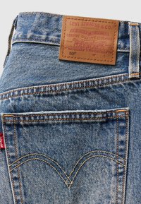 Mėlynos džinsinės kelnės su odiniu etiketė, kurioje pavaizduotas prekės ženklas. Išskirtinė siuvinėjimas ant užpakalinių kišenių ir klasikinis siaurėjantis siluetas.