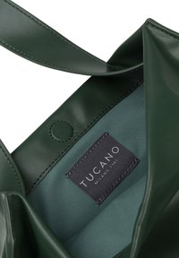 Sac à main en cuir vert avec une texture lisse, doté d'une fermeture à bouton et d'un intérieur doublé d'un tissu vert plus clair. Étiquette de la marque visible.