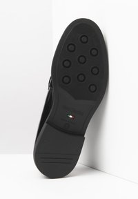 Zwarte leren zool van een schoen met ronde gripaccenten, vlak ontwerp, gestructureerd oppervlak, met een reliëf logo en "Made in Italy" details.