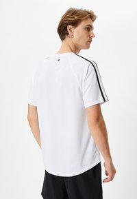 Hvid atletisk t-shirt med korte ærmer, sorte sidestreger, rund nederkant og et lille logo på ryggen ved halsudskæringen. Blød, glat stoftekstur.