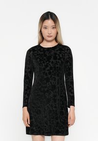 Abito di velluto nero con maniche lunghe, caratterizzato da un motivo floreale testurizzato, scollatura tonda, silhouette aderente e finitura liscia.