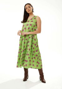 Tiered green dress with purple floral pattern, sleeveless design, falls below the knee, paired with brown cowboy-style boots.
