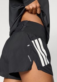 Čierne športové šortky s bielymi pruhmi a logom. Vyrobené z ľahkej tkaniny, majú rozdelený lem a nastaviteľný pás.