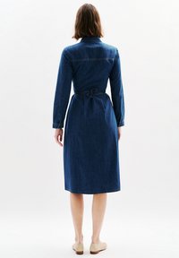 Ciemnoniebieska sukienka dżinsowa z długimi rękawami, kołnierzykiem i zawiązywanym w pasie. Charakteryzuje się długością poniżej kolan i subtelnymi detalami w szwie.